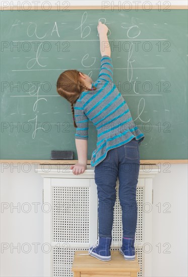 Caucasian girl writing on chalkboard in classroom