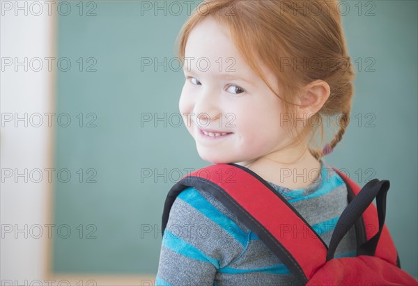 Caucasian girl wearing backpack in classroom