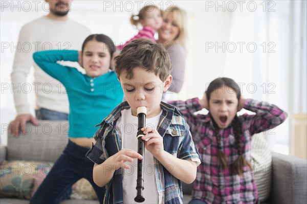 Caucasian family covering ears with boy playing recorder