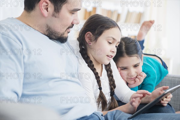 Caucasian father and daughters using digital tablet on sofa