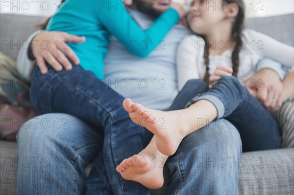 Caucasian father and daughters hugging on sofa