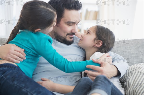 Caucasian father and daughters hugging on sofa