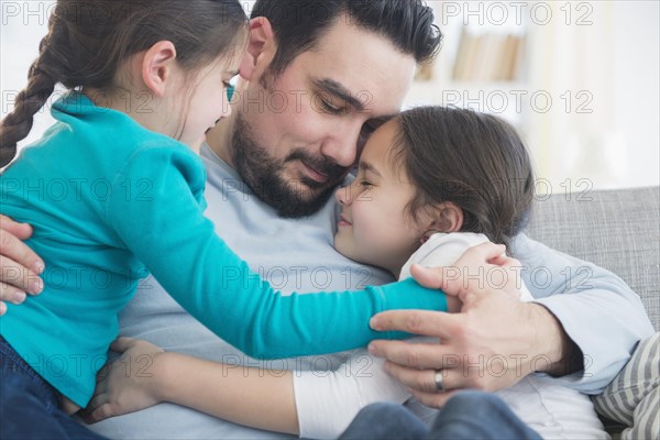 Caucasian father and daughters hugging on sofa