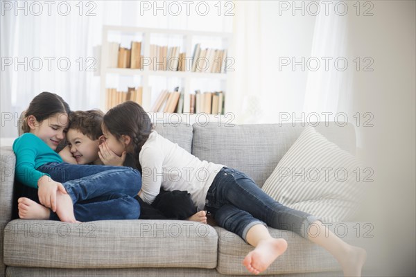 Caucasian brother and sisters whispering on sofa