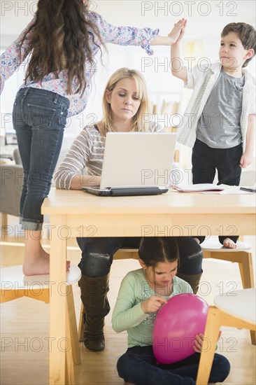 Caucasian mother using laptop with chaotic children