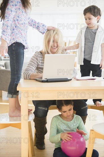 Caucasian mother using laptop with chaotic children