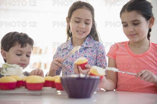 Caucasian siblings spreading frosting on cupcakes