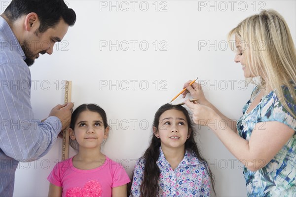 Caucasian parents measuring height of daughters on wall