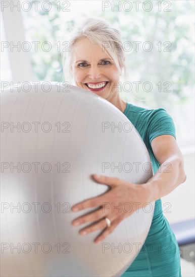 Older Caucasian woman holding exercise ball in gym