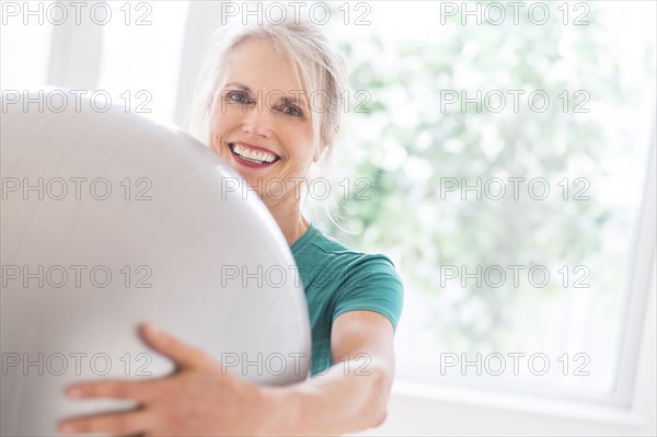 Older Caucasian woman holding exercise ball in gym