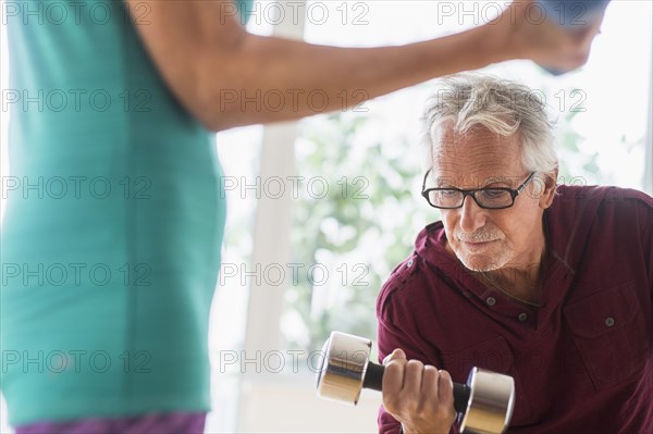 Older Caucasian couple lifting weights in gym