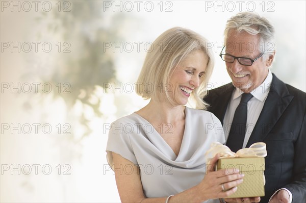 Smiling older Caucasian man giving wife a gift