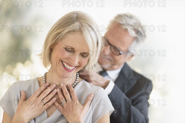 Smiling older Caucasian man giving wife a necklace