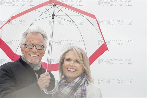 Older Caucasian couple standing under umbrella