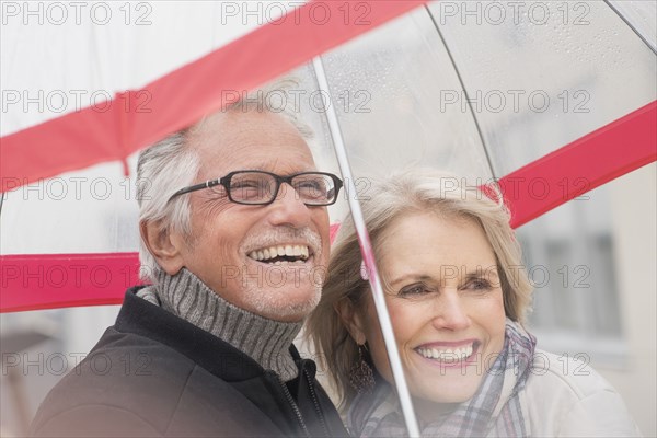 Older Caucasian couple standing under umbrella