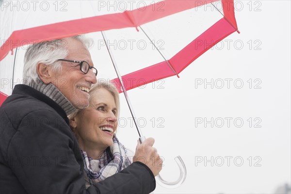 Older Caucasian couple standing under umbrella