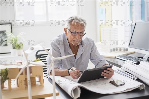 Older Caucasian architect using digital tablet in office