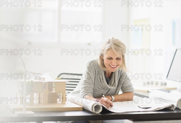 Older Caucasian architect writing on blueprints in office