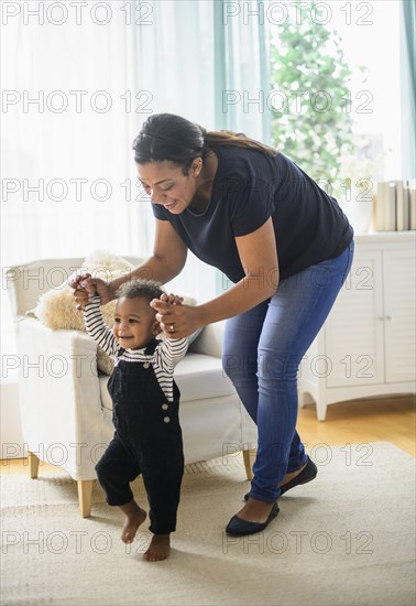 Mixed race mother helping baby son walk in living room