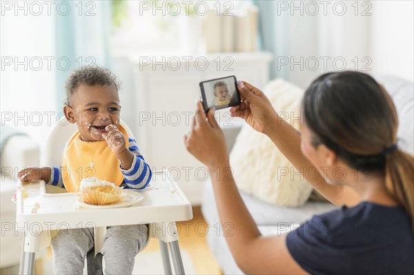 Mixed race mother photographing messy baby boy in high chair