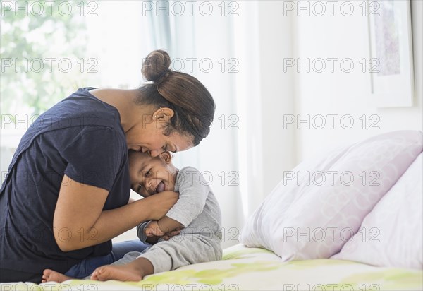 Mixed race mother tickling baby son on bed