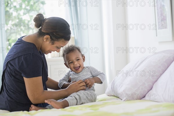 Mixed race mother tickling baby son on bed