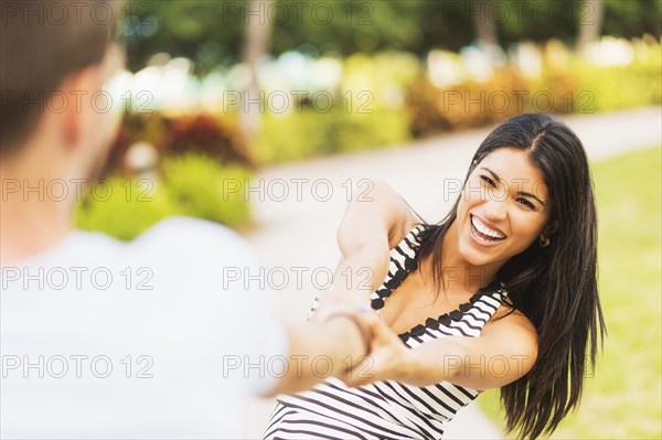 Smiling Hispanic woman pulling boyfriend in park