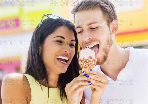 Hispanic couple sharing ice cream cone outdoors