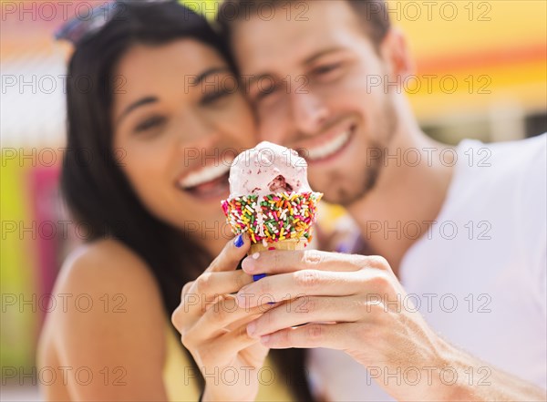 Hispanic couple sharing ice cream cone outdoors