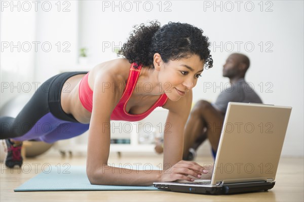 Woman using computer and doing push-ups in gym