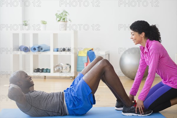 Man doing sit-ups with trainer in gym