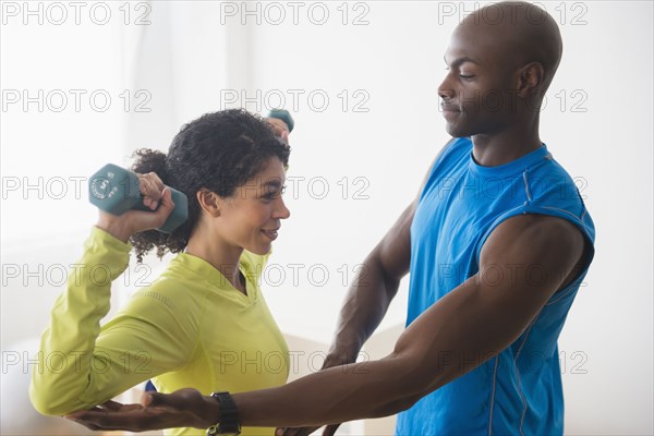 Woman lifting weights with trainer in gym