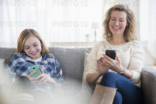 Caucasian mother and daughter using cell phones on sofa