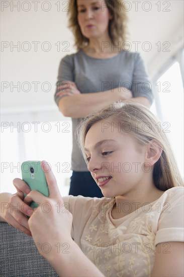 Caucasian mother watching daughter use cell phone