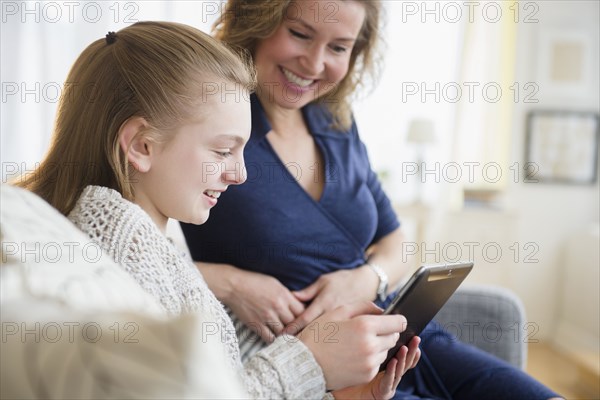 Caucasian mother and daughter using digital tablet on sofa