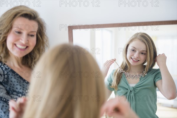 Caucasian girl examining necklace in mirror with mother