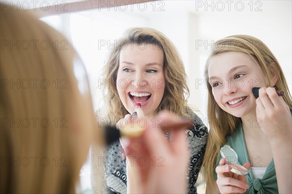 Caucasian mother and daughter applying makeup in mirror