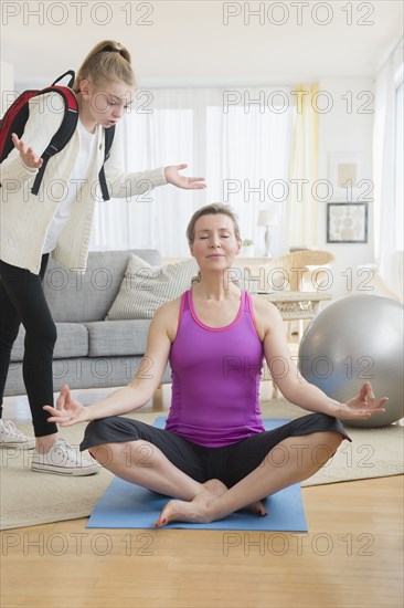 Caucasian daughter annoying meditating mother in living room