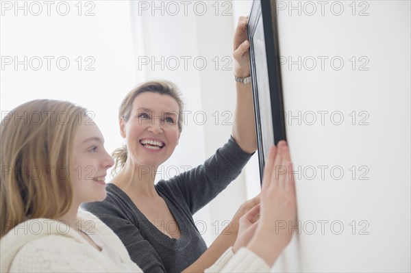 Caucasian mother and daughter hanging picture on wall