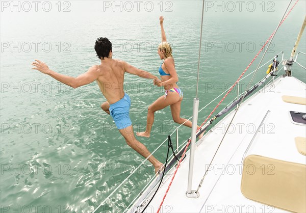 Couple jumping from sailboat deck into ocean