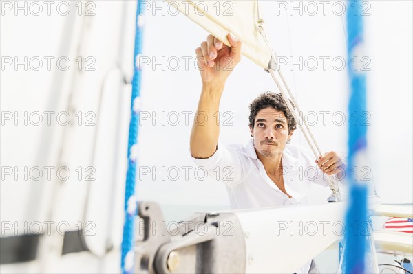 Hispanic man adjusting rigging on sailboat
