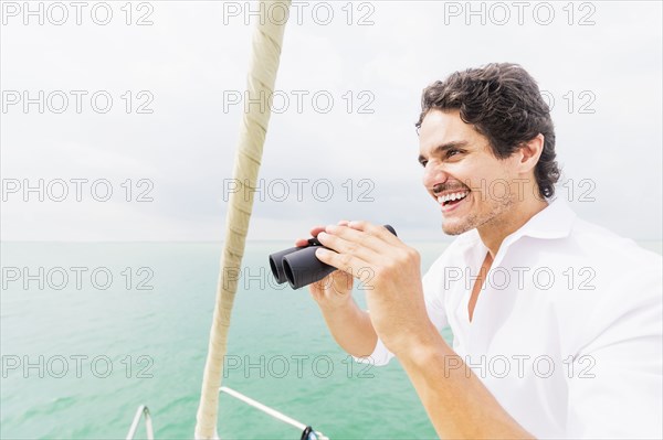 Hispanic man looking out from boat deck with binoculars