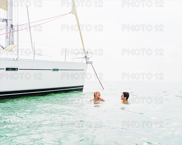 Couple swimming near sailboat