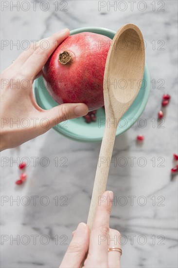 Close up of hands cracking pomegranate with spoon