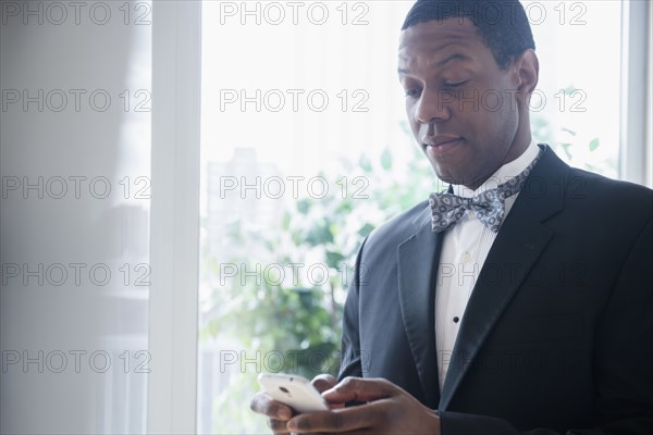 Groom in tuxedo using cell phone