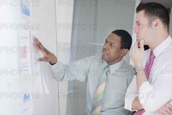 Businessmen examining charts on office wall