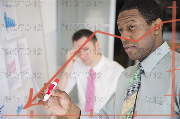 Businessman writing graph on glass wall in office