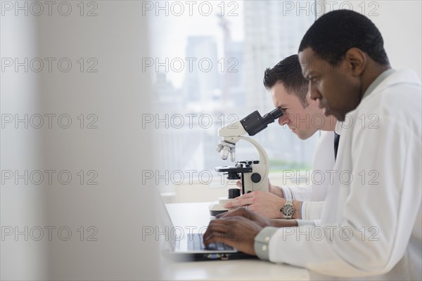 Scientists using laptop and microscope in lab