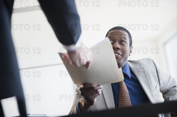 Businessman handing folder to boss in office