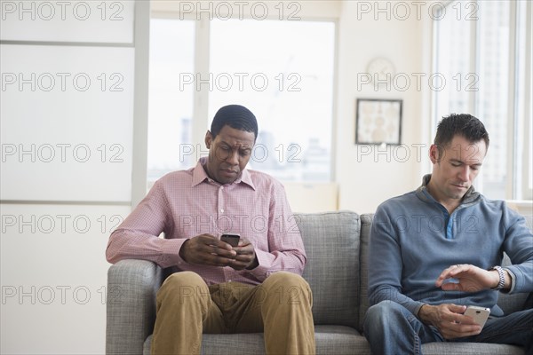 Men with cell phones waiting on sofa